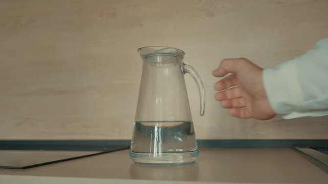 A hand placed a clear jug of water on the table.