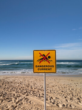 No swimming dangerous current sign at beach on perfect sunny day with blue sky and waves in vertical format..