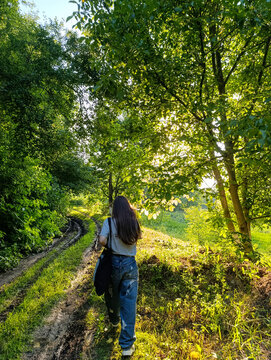 Back View of Young Woman Walking Along Dirt Path in Forest
