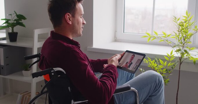 Man seated in wheelchair to make distant video call, happy patient looking at laptop screen communicating with doctor therapist online, using modern tech application for faster rehabilitation