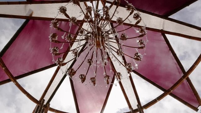 Crystal chandelier hangs beneath a circular tensile pavilion with translucent fabric canopy and timber framework in Chapada dos Veadeiros, Alto Paraiso de Goias, Goias, Brazil, tilt up.