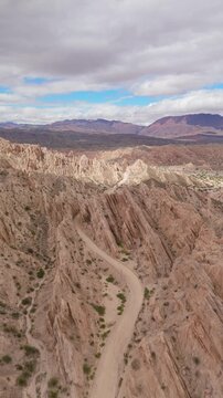 Winding sandy road cuts through fractured cliffs in Quebrada de las Flechas, Argentina, aerial vertical