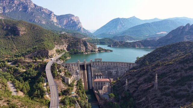 Panoramic view of Oliana dam in Lleida, Catalonia, with stepped concrete spillway, arched crest, powerhouse, electrical substation, motorway viaduct and pre-Pyrenean mountains