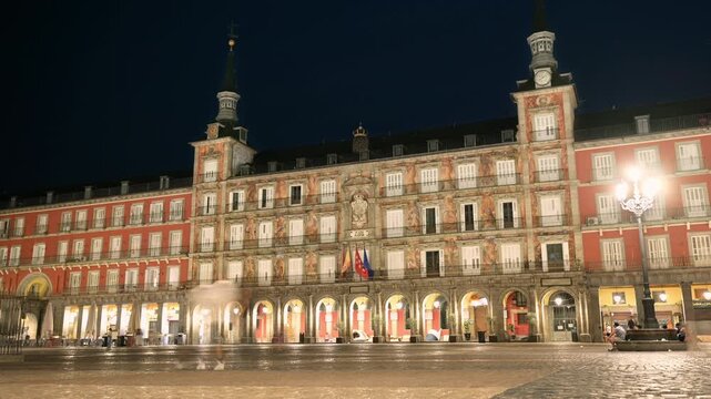 Night time lapse of Plaza Mayor square in Madrid, Spain, featuring the illuminated historic Casa de la Panaderia facade with motion blur of pedestrians on cobblestones. High quality 4k footage