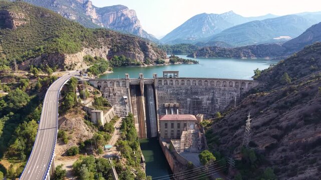 Panoramic view of Oliana dam in Lleida, Catalonia with concrete spillway, arched gallery crest, powerhouse, electrical substation, motorway viaduct and pre-Pyrenean mountains