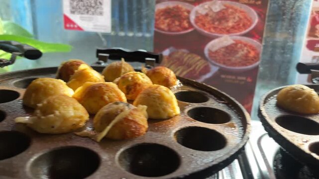 Golden round takoyaki cooking in a specialized hot griddle pan.