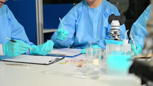 Focused scientists in PPE work together in a modern lab, examining samples and recording critical data for breakthrough research.