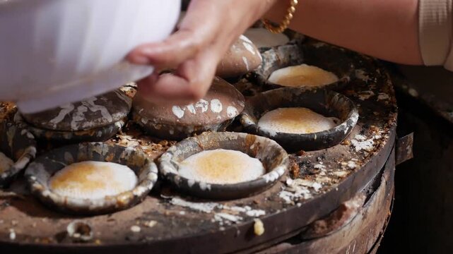 Round molds filled with white batter cook on a work table during preparation of traditional ban can food. Local cuisine.