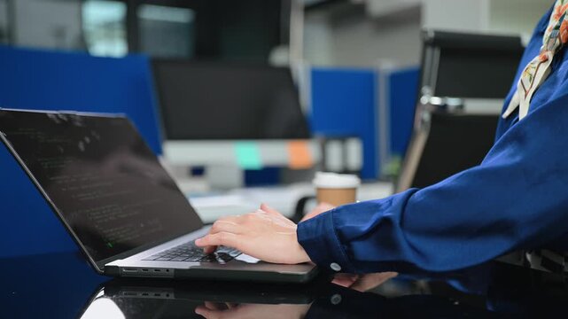 Focused female developer typing code on a laptop in a modern office, highlighting tech innovation and software engineering expertise.