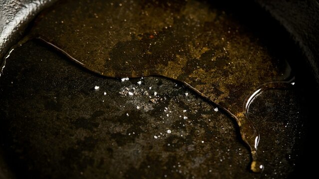 Close-up of dirty cooking pan with oil and food residue on dark surface