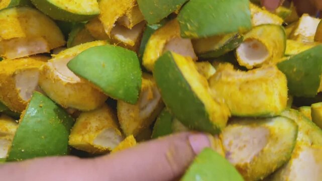 Mixing fresh chopped green mango slices with turmeric powder for traditional Indian pickle preparation.