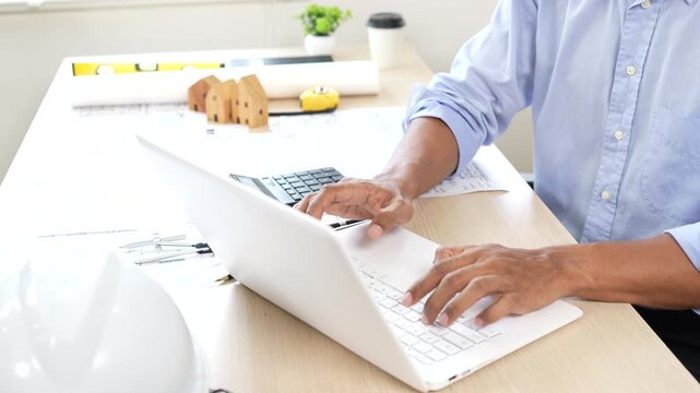 Architect reviewing construction plans at a modern office desk with blueprints, laptop, and engineering tools for a building project.