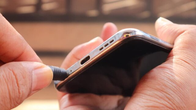 Connecting Audio. Asian man's hand Plugging Wired Earphones into a Smartphone.