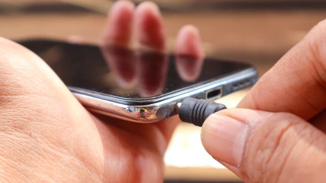 Connecting Audio. Asian man's hand Plugging Wired Earphones into a Smartphone.