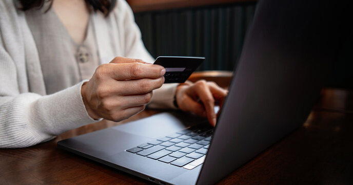 Woman holding a credit card while using a laptop for online shopping at cafe. Conceptual image representing e-commerce, digital payment.