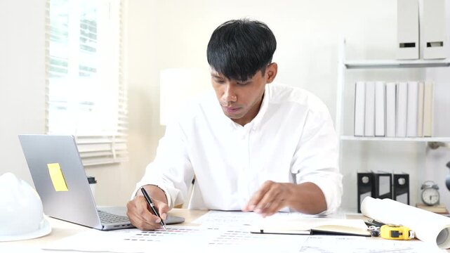 Architect reviewing construction plans at a modern office desk with blueprints, laptop, and engineering tools for a building project.