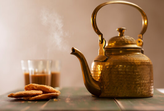 Brass kettle blowing hot air kept next to matthis and three glasses filled with tea on a table