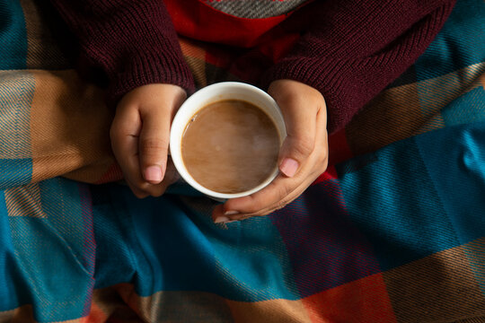 Woman in a blanket feeling the warmth of hot tea in her hand during winter