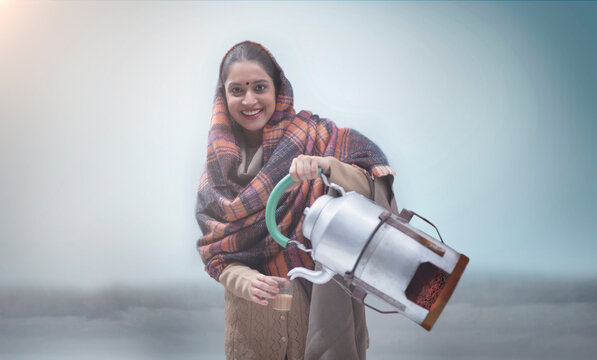 Woman with a kettle attached to an angeethi serving tea