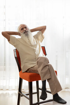 A BEARDED OLD MAN SITTING ON CHAIR AND THINKING