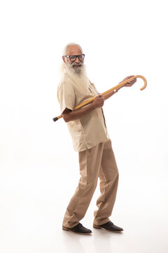 A HAPPY OLD MAN PLAYFULLY HOLDING WALKING STICK AS HE IS PLAYING GUITAR