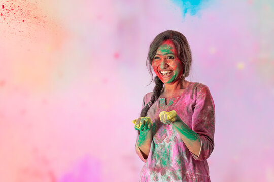 Beautiful woman with colors in her hands and gulal on her face smiling on Holi