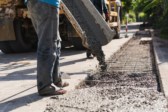 Wet concrete pouring down a mixer truck chute onto sidewalk renovation work.
