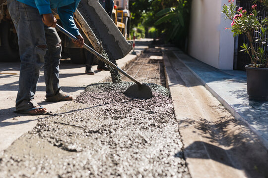 Construction worker using a hoe tool to spread fresh wet concrete from a mixer truck.