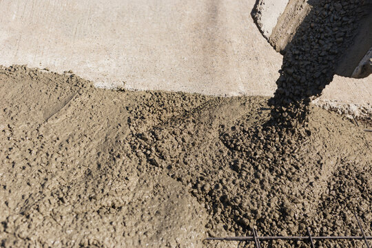 Concrete mixture pouring onto a rebar reinforced ground surface during a road paving project.