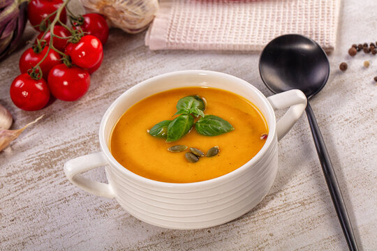Pumpkin cream soup in white bowl with basil and pumpkin seeds