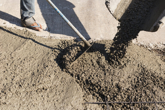 Shot of wet concrete pouring from a chute while a worker spread and level the aggregate