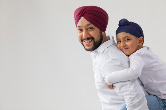 A LITTLE SIKH BOY HUGGING HIS FATHER HAPPILY AND LOOKING AT CAMERA