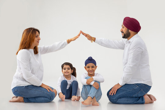 SIKH FATHER AND MOTHER SITTING DOWN AND FORMING SHELTER WITH HANDS WITH SON AND DAUGHTER SITTING BELOW