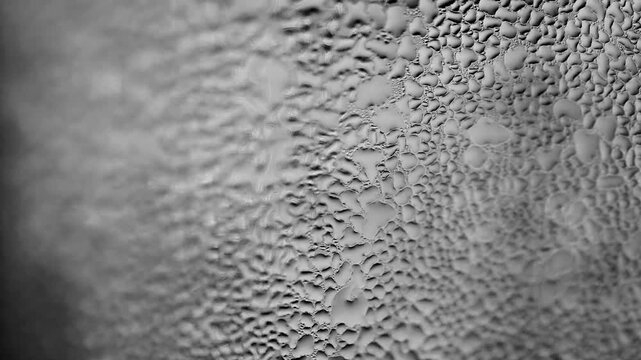 Abstract texture of water droplets on glass, creating a unique and organic pattern. The droplets vary in size and shape, forming an interesting visual effect