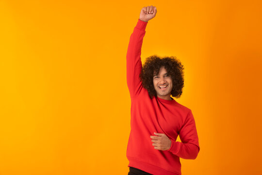 A CURLY HAIRED MAN RAISING HIS FIST HAPPILY IN FRONT OF CAMERA