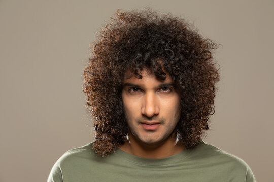 PORTRAIT OF A YOUNG MAN WITH CURLY HAIR SERIOUSLY LOOKING AT CAMERA