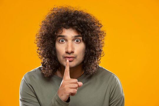 A YOUNG MAN WITH CURLY HAIR GESTURING TO STAY QUIET