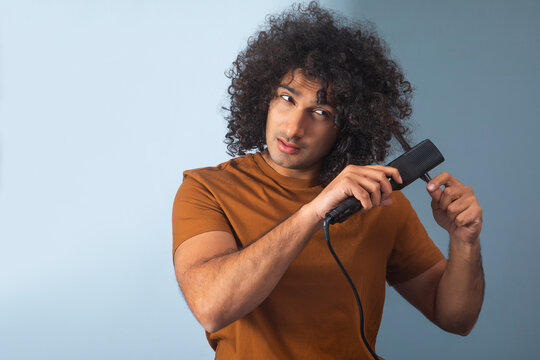 A CURLY HAIRED YOUNG MAN USING A STRAIGHTENER 