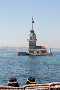 Rear view of two unrecognisable girls wearing daisy chain headbands sitting on the waterfront looking at the Maiden's Tower (Leander's Tower) across the Bosphorus, Istanbul, Turkey