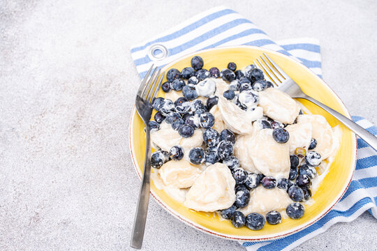 Overhead view of a plate of Traditional Ukrainian dumplings stuffed with cottage cheese (varenyky), sour cream and blueberries on a table with a napkin and cutlery