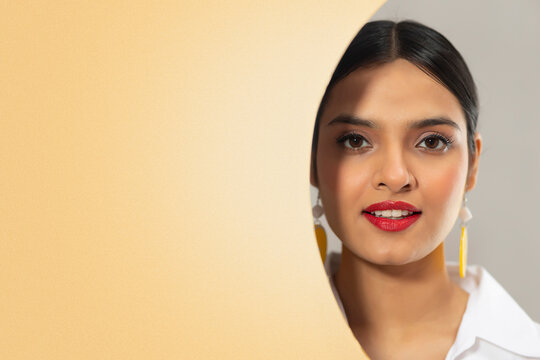 PORTRAIT OF A YOUNG WOMAN LOOKING AT CAMERA FROM BEHIND A CUTOUT WALL