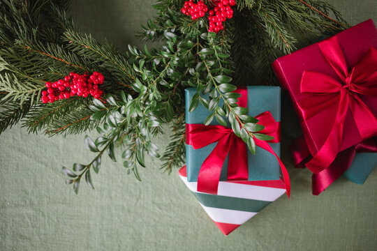 Close-up overhead view of wrapped Christmas gifts decorated with red satin ribbons and assorted foliage with berries on a table