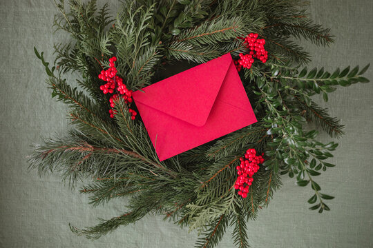 Overhead view of a blank red paper envelope on a handmade Christmas wreath on a table