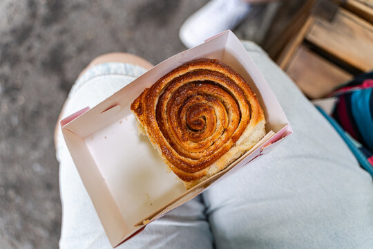 Close-up overhead view of a teenage boy sitting in a park eating a cinnamon roll in a cardboard box