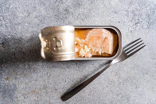 Close-up overhead view of an open tin of canned salmon and a fork on a concrete worktop