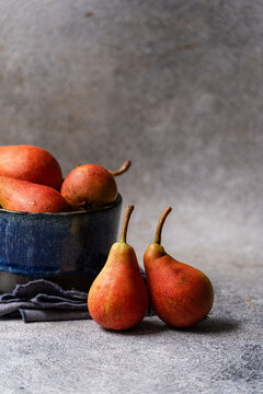 Close-up of two ripe pears next to a cup of pears on a grey ceramic worktop