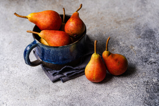 Close-up of two ripe pears next to a cup of pears on a grey ceramic worktop