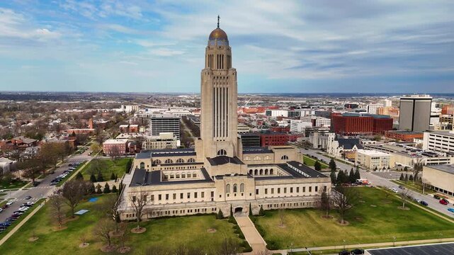 Majestic drone footage of the Nebraska State Capitol in Lincoln, Nebraska, USA, featuring the iconic government tower topped with The Sower statue, surrounded by downtown streets 
