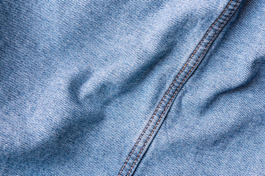 Blue denim seam fabric texture background with copy space. Minimalist jeans cloth banner featuring contrast stitching and soft folds.