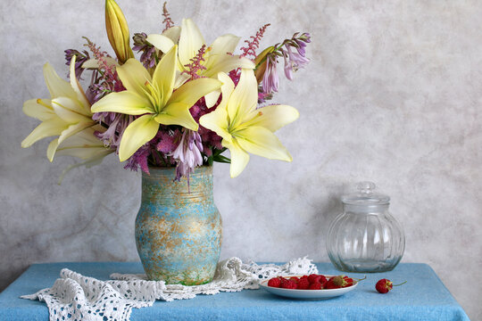 lily flowers and astilbe bouquet stand in ceramic vase on blue tablecloth with fresh red raspberries. floral still life arrangement for home interior decoration.